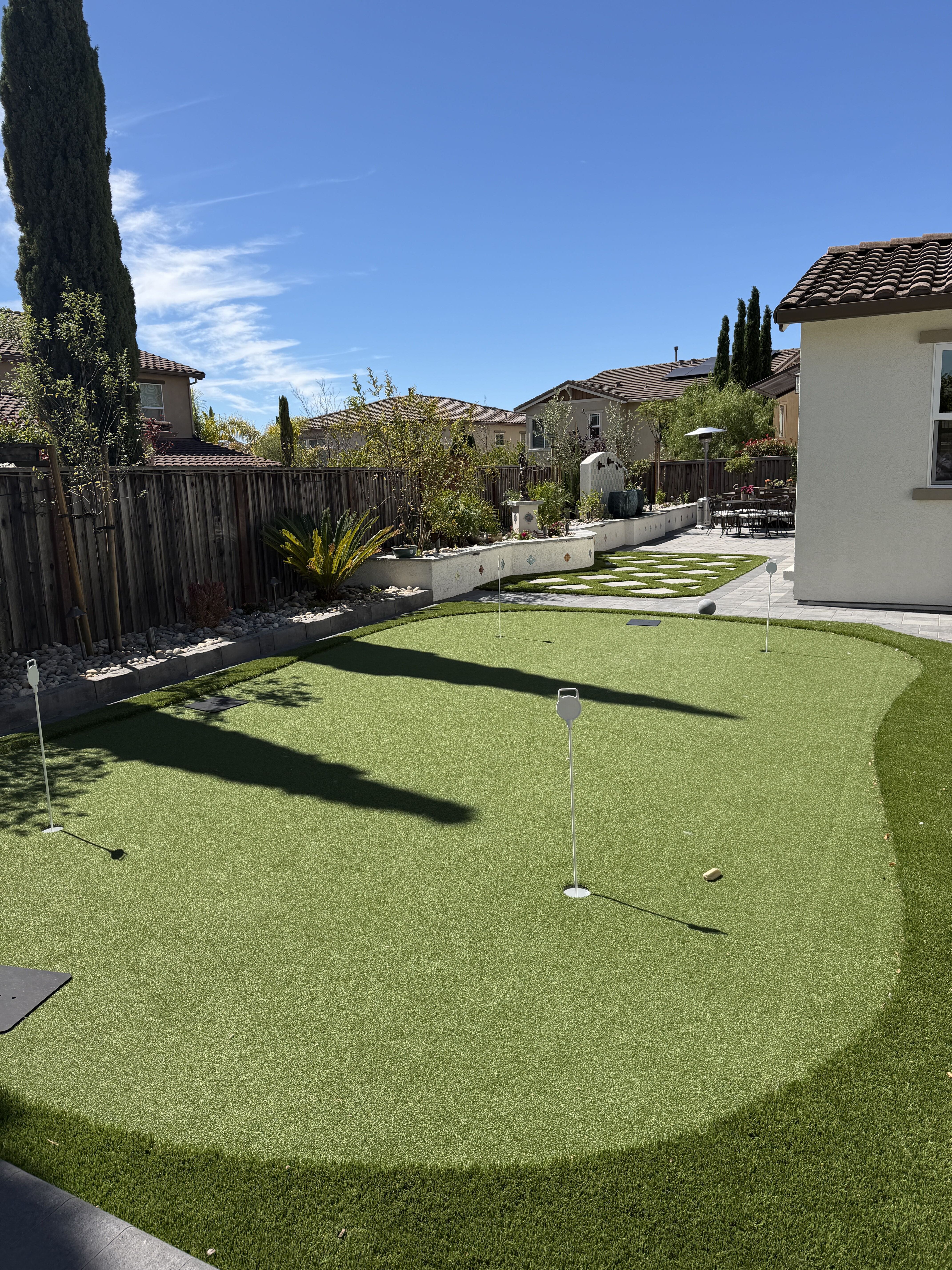 Dublin putting green and connecting walkway Artificial-turf putting green with golf flags beside a paved walkway and geometric steppers in the finished Dublin backyard.