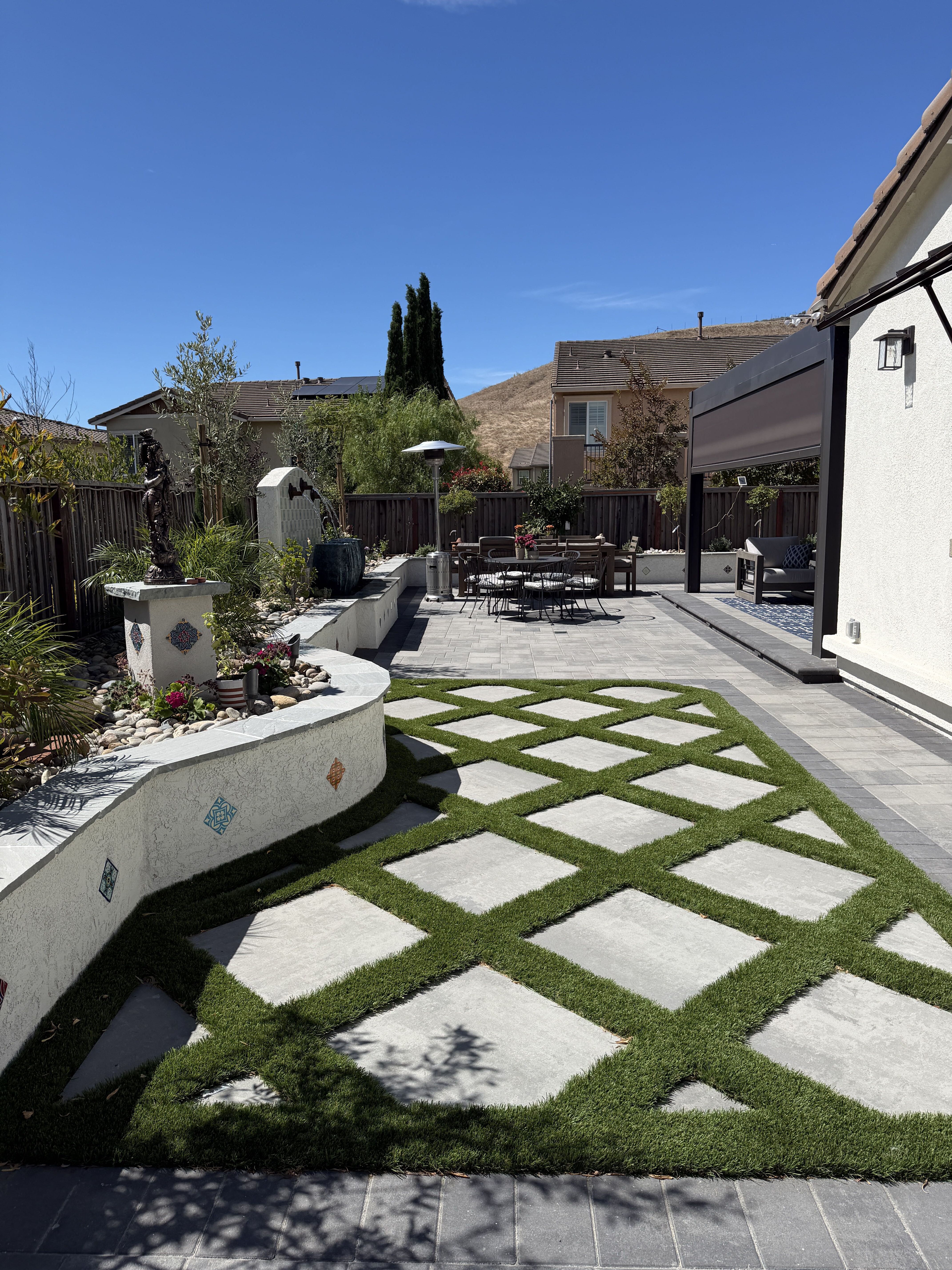 Dublin patio and geometric turf steppers Geometric paving set in artificial turf leads past curved planted walls toward the backyard patio and seating area.